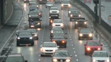 Yağmurda trafik sıkışık. Otoyolda birden fazla araba ve motosiklet yavaş sürüyor.