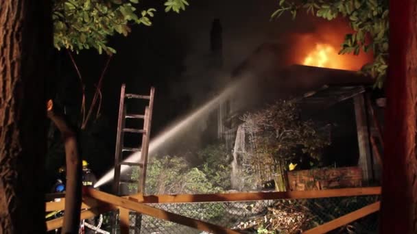 夜に家の上で燃える火に水をかける正体不明の消防士 — ストック動画