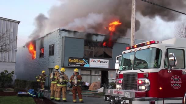 三人の消防士がビルの角の前に立ち窓から炎を上げながら — ストック動画