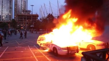 Çevik kuvvet polisleri Vancouver ayaklanması sırasında iki polis arabasının arkasında kalabalığı dağıtıyor.