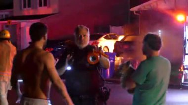 Montreal SPVM polis memuru vatandaşlarla konuşurken arkada bir araba yanıyor
