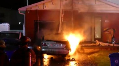 Arabadan çıkan alev ve duman, hasarlı bir evin yakınında alevleniyor.