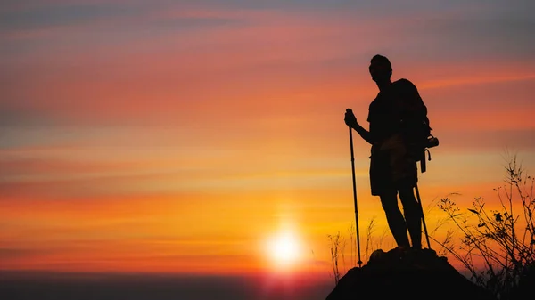 İnsan yürüyüşçüsünün silueti güneşli kayalık dağ zirvesinde duruyor — Stok fotoğraf