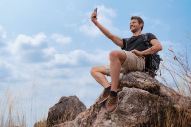 Adam yürüyüşçüsü mavi gökyüzü arka planında kayanın üstünde selfie çekiyor.