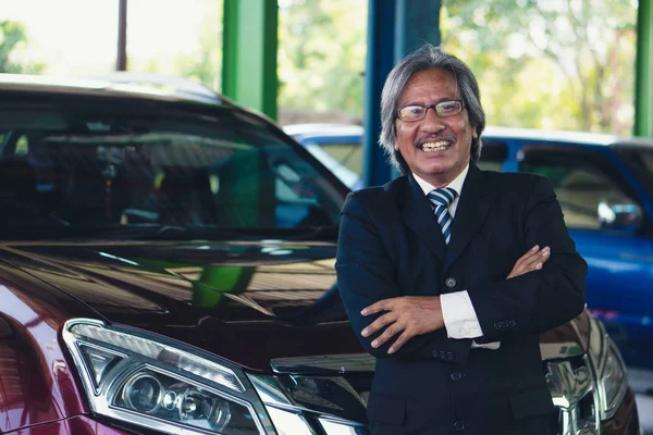 portrait of happy elder customer with his car at garage and car