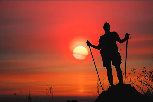 İnsan yürüyüşçüsünün silueti güneşli kayalık dağ zirvesinde duruyor — Stok fotoğraf