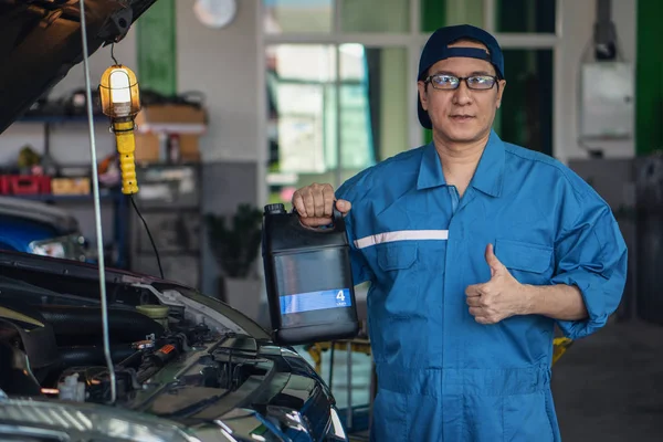portrait of car mechanic with engine oil pack at garage and car