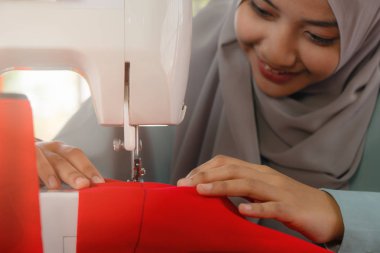 Onu dikiş makinesi kullanan Müslüman moda tasarımcısının elleri.