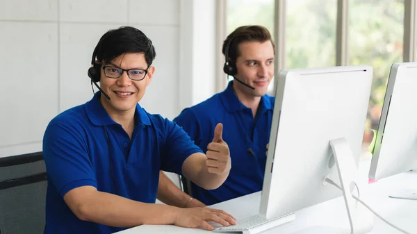 business background of asian and caucasian male customer service agents on telephone service to customers at helpdesk call center and customer service operation center