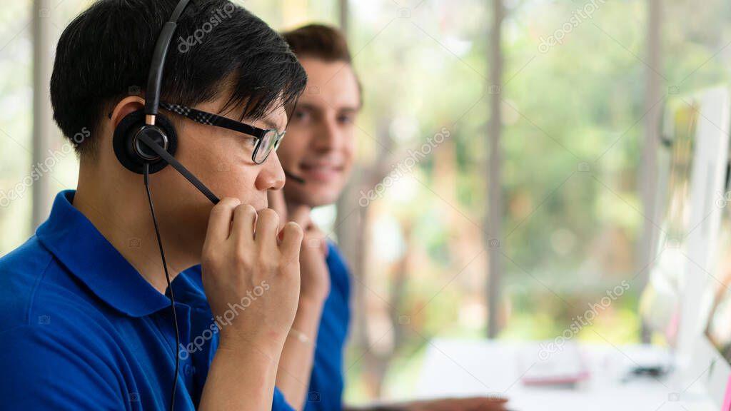 business background of asian and caucasian male customer service agents on telephone service to customers at helpdesk call center and customer service operation center