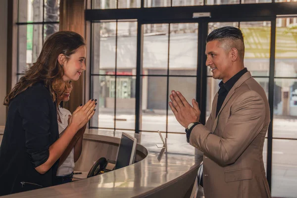 guest and hotel receptionist having greeting with thai wai in order to keep social distance in coronavirus covid 19 world pandemic, greeting culture in coronavirus covid 19 pandemic situation