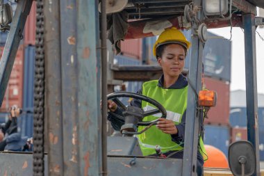 Afrika kökenli Amerikan forklift sürücüsü konteynır deposu ve kargo deposunda forklift kullanıyor.