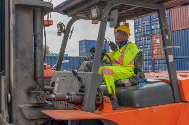 Afrika kökenli Amerikan forklift sürücüsü konteynır deposu ve kargo deposunda forklift kullanıyor.