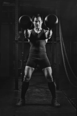 Asyalı atletik güçlü adam spor yapıyor ve kettlebell halterli vücut geliştiriyor spor salonunda ağırlık kaldırıyor ve spor salonunda siyah-beyaz renkte spor yapıyor.