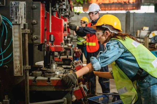 Asyalı kadın ve erkek imalat işçileri metal üretim fabrikası doğrultusunda birlikte çelik sondaj makinesi işletiyorlar.