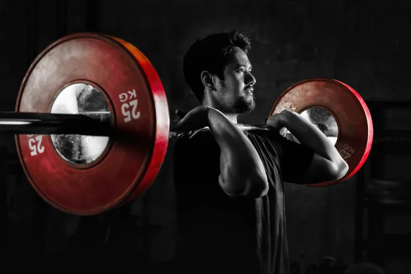 Asyalı atletik güçlü bir adam spor yapıyor ve halterli vücut geliştiriyor. Spor salonunda ağırlık kaldırıyor ve spor salonunda koyu renkli iki tonda spor yapıyor.