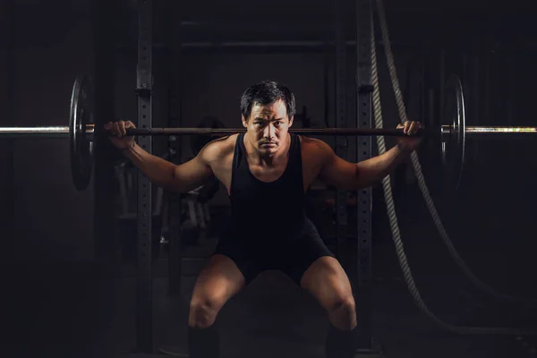 アジア運動能力の強い男がトレーニングやボディビルを持っていますとともにバーベル重量挙げバックスクワットスタイルでジムやフィットネスセンターで暗いトーン — ストック写真