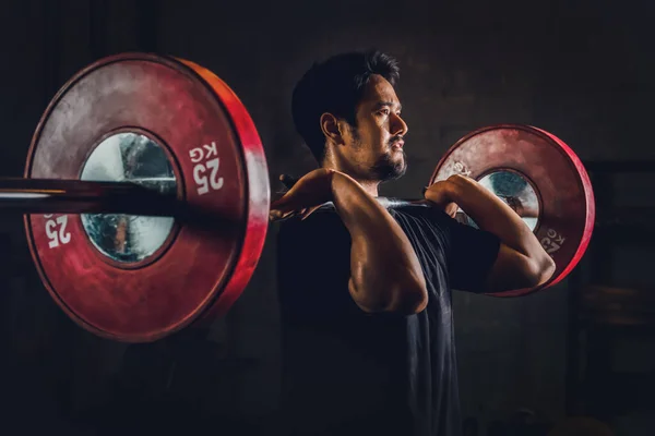 Asyalı atletik güçlü adam vücut geliştiriyor ve ağırlık kaldırıyor spor salonunda ağırlık kaldırıyor ve spor salonunda koyu renk tonda spor yapıyor.