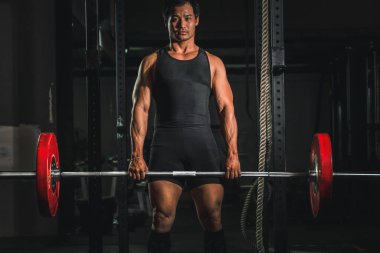 Asyalı atletik güçlü adam vücut geliştiriyor ve vücut geliştiriyor. Spor salonunda ağırlık kaldırma stili, spor salonunda spor salonu ve spor salonunda koyu tonda spor yapıyor.