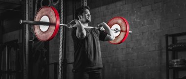 Asyalı güçlü atletik adam spor yapıyor ve vücut geliştiriyor halterlerle ağırlığını ön tarafa veriyor. Spor salonunda stil ve spor salonunda iki ton koyu renk.