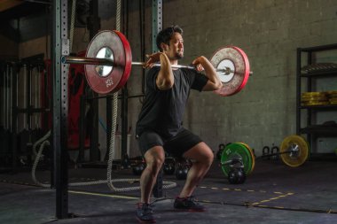 Asyalı güçlü atletik adam spor yapıyor ve vücut geliştiriyor halterlerle ağırlık kaldırıyor spor salonunda ve spor salonunda siyah tonda stil belirliyor.