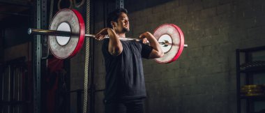 Asyalı güçlü atletik adam spor yapıyor ve vücut geliştiriyor halterlerle ağırlık kaldırıyor spor salonunda ve spor salonunda siyah tonda stil belirliyor.