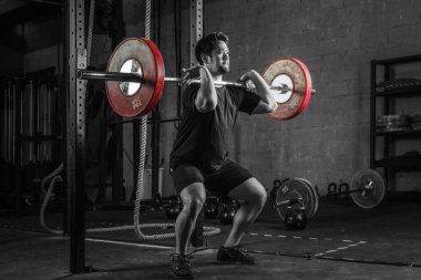 Asyalı güçlü atletik adam spor yapıyor ve vücut geliştiriyor halterlerle ağırlığını ön tarafa veriyor. Spor salonunda stil ve spor salonunda iki ton koyu renk.