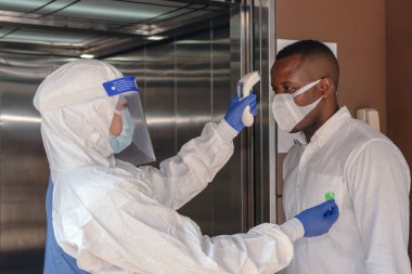 Coronavirus covid-19 'daki koruma görevlisi ofis binasına girmeden önce Afro-Amerikan iş adamını kontrol etmek için dijital ısı tarama cihazı kullanıyor.