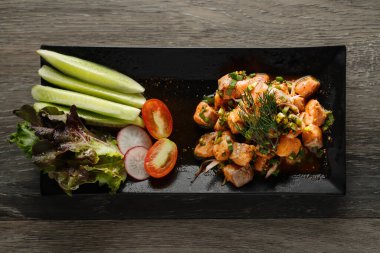 Tayland usulü baharatlı çiğ somon salatasının sağlıklı yemek arkaplanı siyah tabakta salatalık, salatalık turpu ve dilimlenmiş salatalık ile servis edilir.