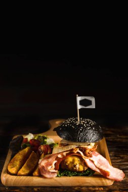 Amerikan yemeği arka planında sığır eti ve pastırma siyah hamburgerler, siyah tabakta koyu tonda, ince odaklı.