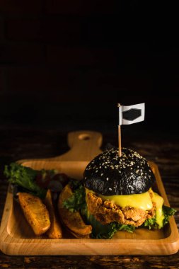 Koyu tonda, ahşap tabakta salata soslu kızarmış tavuk siyah hamburgerinin Amerikan yemeği arka planı.