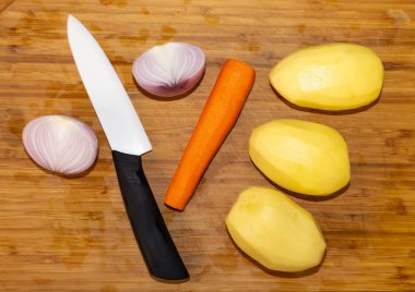 Soyulmuş patates, soğan ve havuç ve beyaz seramik bıçaklı bir bıçakla ahşap kesim tahtası manzarası