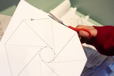Origami zanaatı yapmak için işaretli bir kağıdı makasla kesen bir kadının görüntüsü