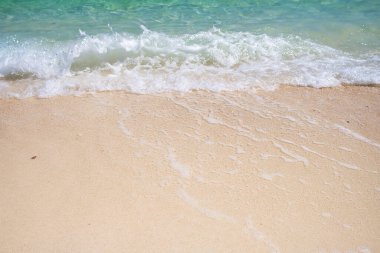 Temiz kumsalda yumuşak mavi okyanus dalgaları. Mavi deniz kumdaki yumuşak dalgalar sürekli ve güzel bir şekilde kıyıya dokunuyor.
