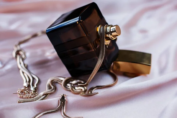 Frasco de perfume com colar de ouro em fundo rosa — Fotografia de Stock