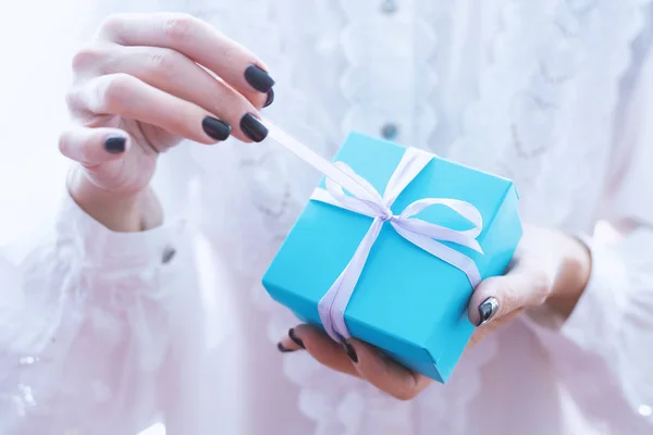 Manos femeninas sosteniendo un pequeño regalo envuelto con cinta rosa. Mala. — Foto de Stock