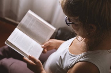 Yaşlı kadın evde kitap okuyor.