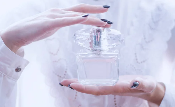 Las manos femeninas sostienen el perfume sobre un fondo claro — Foto de Stock