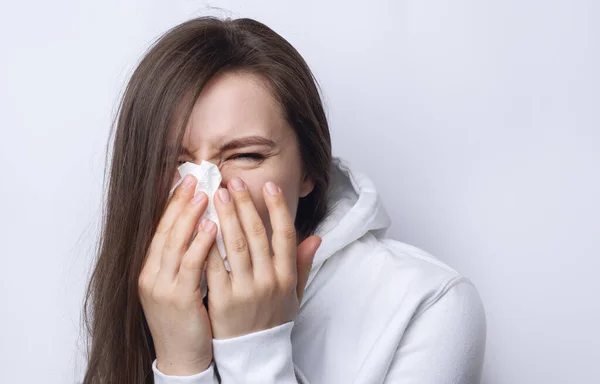 Cold young woman sneezes into a napkin