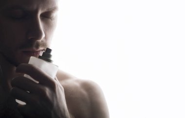 Yakışıklı genç adam, beyaz arka taraftaki parfüm şişesini kokluyor.