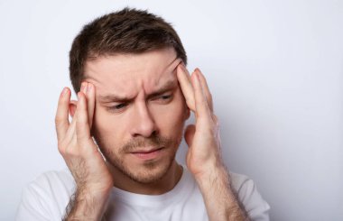 Şiddetli baş ağrısından muzdarip gri arka planda izole edilmiş genç bir adamın portresi şakaklara parmak bastırıyor.