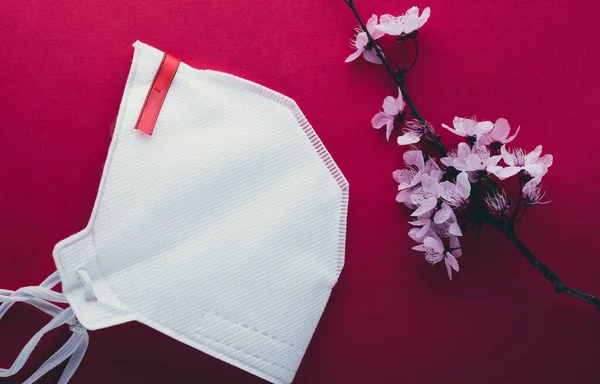 Medical concept on a pink background. Medical mask and a branch of spring flowers as a symbol of hope.