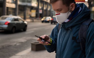 Sokaktaki tıbbi maskeli adam akıllı telefon kullanıyor.