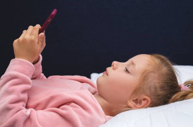 çocuk, teknoloji ve internet kavramı - küçük kız evde akıllı telefonuyla yatakta yatıyor