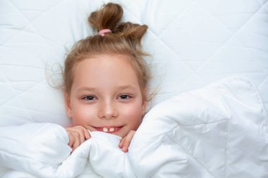 Beyaz yastıkla yatakta uzanan sevimli, sevimli, beyaz, beyaz, beyaz, sarışın küçük kız.
