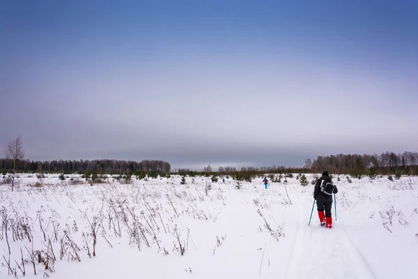 Tourists walk along a snow-covered winter field. — Stock Photo, Image