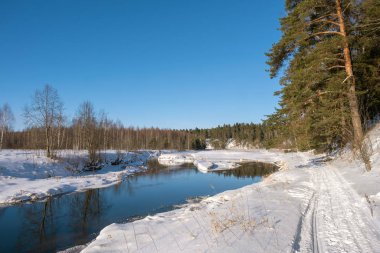 Kışın güneşli bir günde ve mavi gökyüzünde küçük bir nehir manzarası.