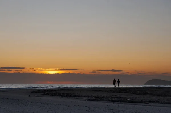 Vista al amanecer y silueta de pareja caminando por la playa — Foto de Stock