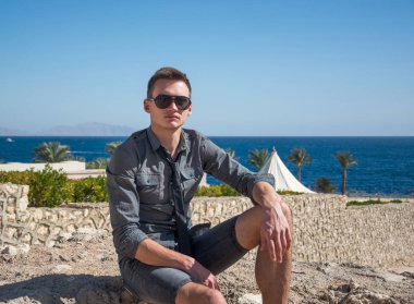 Yaz aylarında deniz kenarında güneş gözlüklü adam oturur