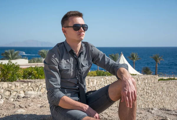 Man in sunglasses sits near the sea in summer time — Stock Photo, Image